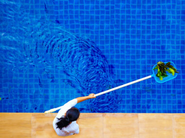Femme ramassant les feuilles dans une piscine à l'aide d'un manche et d'une épuisette, vue du dessus