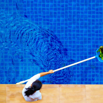 Femme ramassant les feuilles dans une piscine à l'aide d'un manche et d'une épuisette, vue du dessus