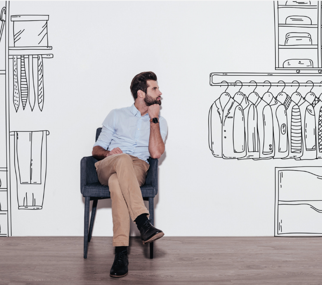 Jeune homme assis avec dessins de penderies et d'étagères sur le mur blanc derrière lui