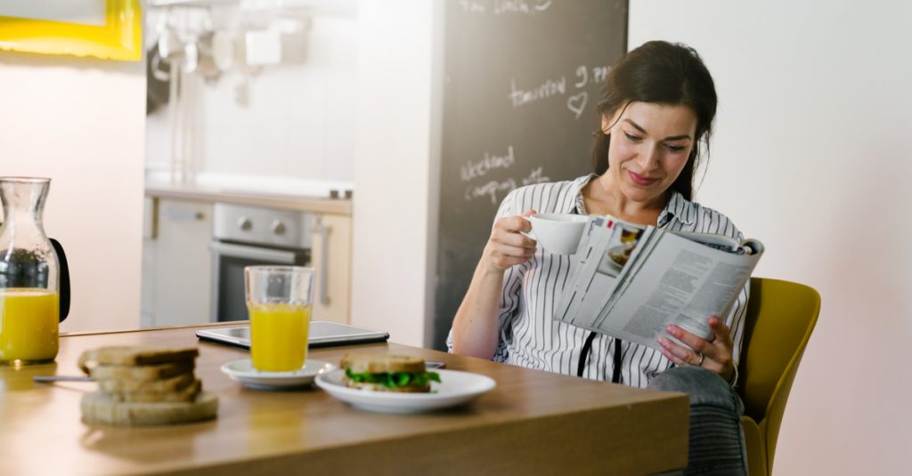 Femme en train de lire en prenant son petit déjeuner avant sa journée de télétravail