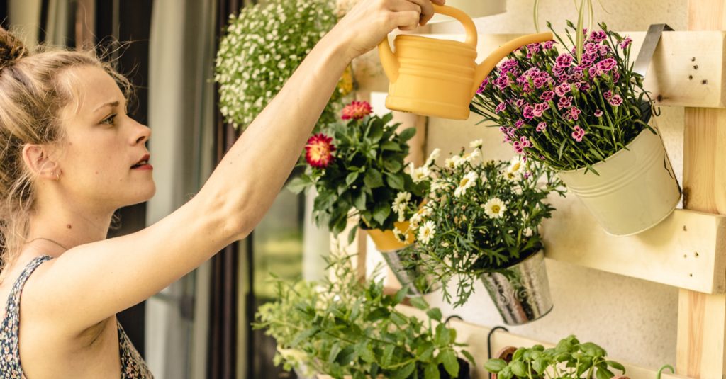 Jeune femme arrosant des pots de fleurs suspendus sur le mur du balcon