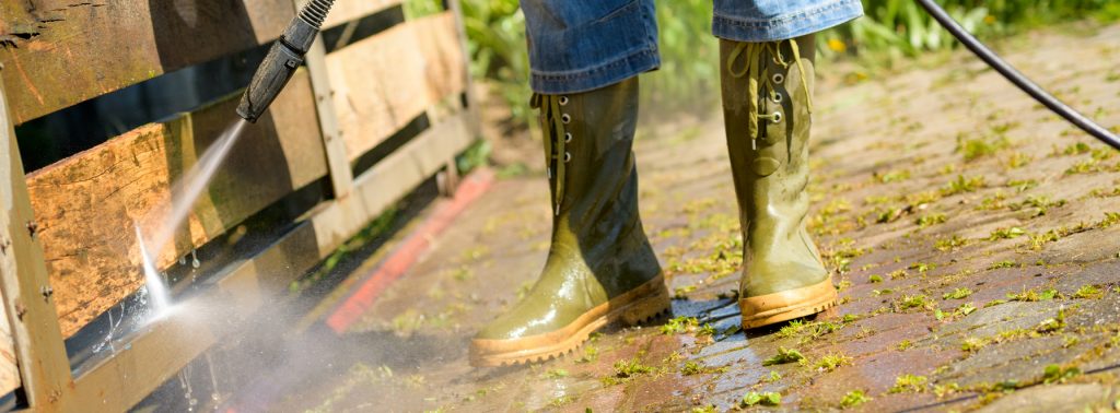 Personnes en bottes de pluie en train de nettoyer sa terrasse en bois au jet d’eau