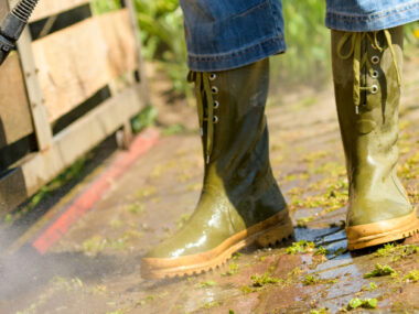 Personnes en bottes de pluie en train de nettoyer sa terrasse en bois au jet d’eau