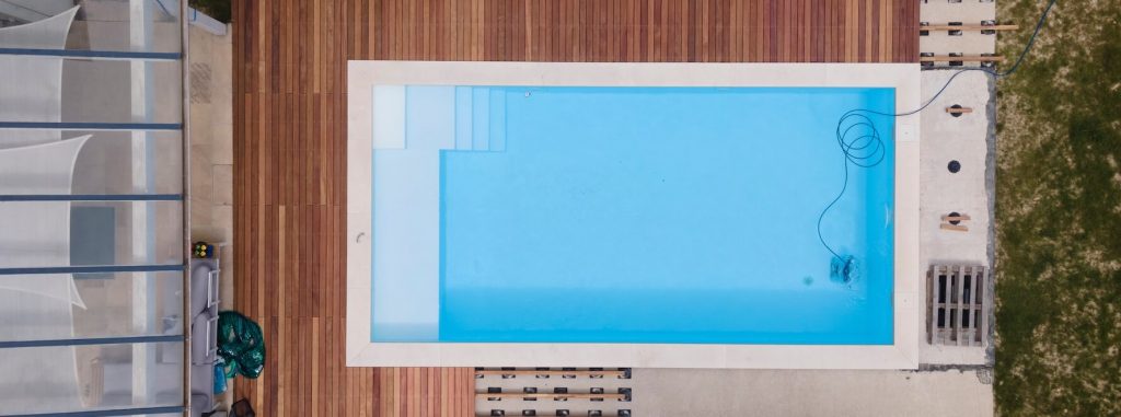 Piscine au sel ou au chlore ? Votre comparatif complet Piscine avec terrasse en bois vue aérienne